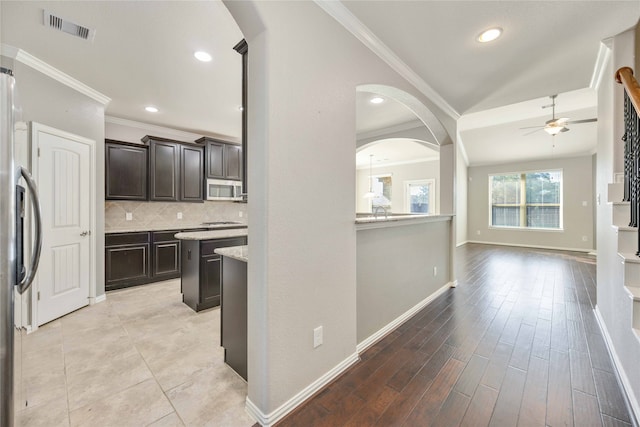 kitchen featuring dark brown cabinetry, crown molding, light hardwood / wood-style floors, decorative backsplash, and appliances with stainless steel finishes