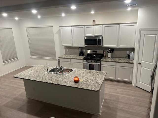 kitchen featuring light stone counters, light hardwood / wood-style floors, appliances with stainless steel finishes, and a center island with sink