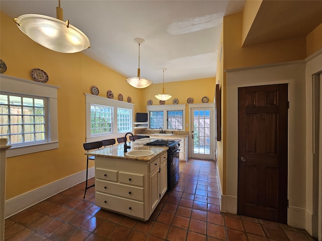 kitchen featuring sink, hanging light fixtures, black range with gas stovetop, a kitchen bar, and a kitchen island with sink