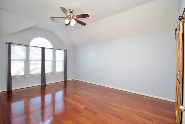 spare room with a barn door, ceiling fan, dark hardwood / wood-style floors, and vaulted ceiling