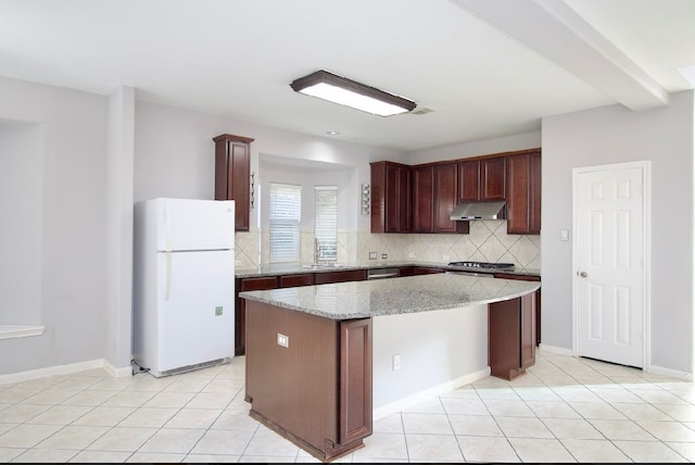 kitchen with light tile patterned floors, white refrigerator, a kitchen island, and light stone counters