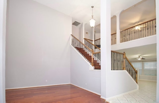 stairs with ceiling fan, wood-type flooring, and a high ceiling