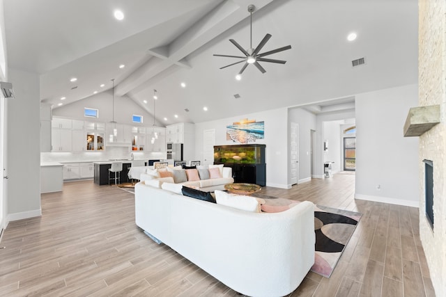 living room featuring high vaulted ceiling, ceiling fan, light hardwood / wood-style floors, a fireplace, and beam ceiling