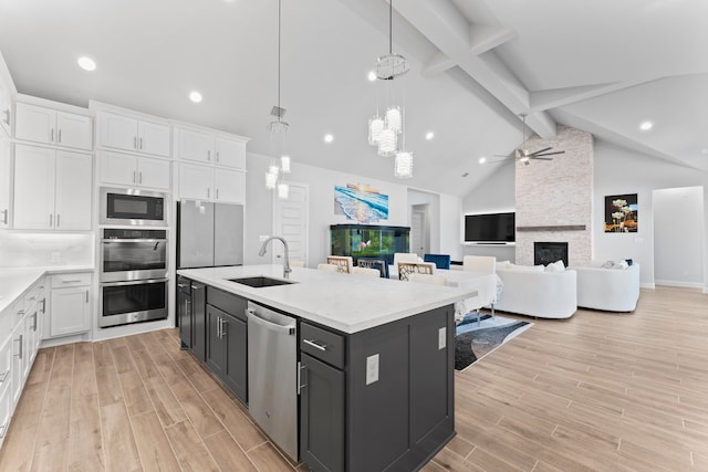 kitchen featuring white cabinetry, stainless steel appliances, a stone fireplace, pendant lighting, and a center island with sink