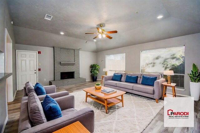 living room with lofted ceiling, light wood-type flooring, a fireplace, and ceiling fan