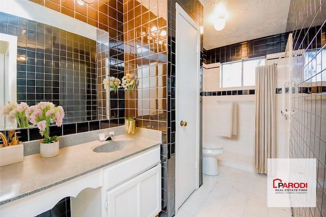 bathroom with tile walls, toilet, vanity, and tile patterned flooring