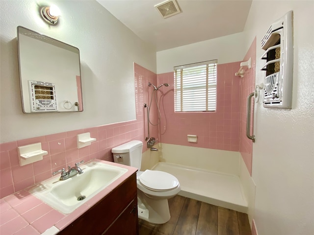 bathroom featuring vanity, hardwood / wood-style flooring, toilet, tiled shower, and tile walls