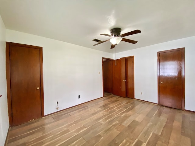 unfurnished bedroom with ceiling fan, two closets, and light wood-type flooring