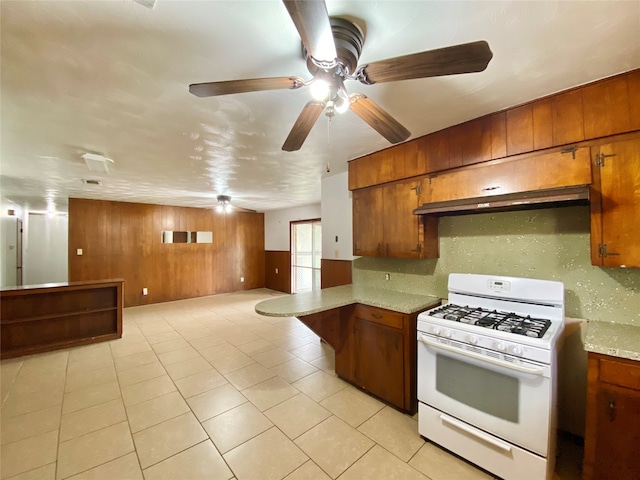 kitchen featuring backsplash, gas range gas stove, light tile patterned floors, and wood walls