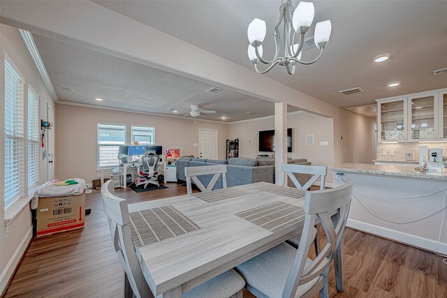 dining room featuring wood-type flooring, ceiling fan with notable chandelier, and crown molding