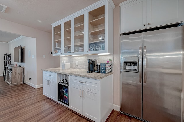 kitchen featuring stainless steel refrigerator with ice dispenser, light wood-type flooring, backsplash, light stone counters, and white cabinets