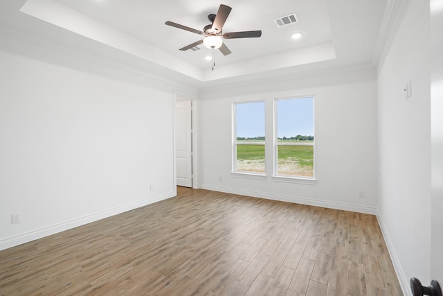 empty room with ceiling fan, crown molding, a tray ceiling, and light hardwood / wood-style flooring