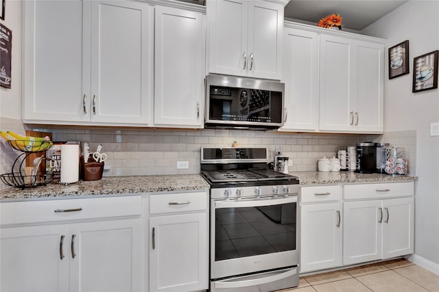 kitchen with white cabinetry, light stone counters, backsplash, light tile patterned floors, and appliances with stainless steel finishes