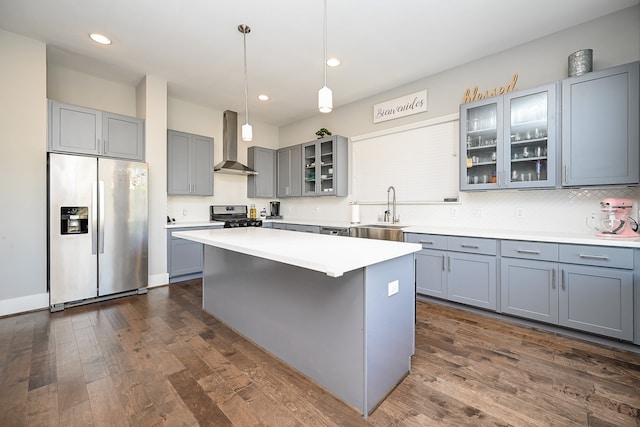 kitchen with dark wood-type flooring, wall chimney range hood, sink, decorative light fixtures, and stainless steel appliances