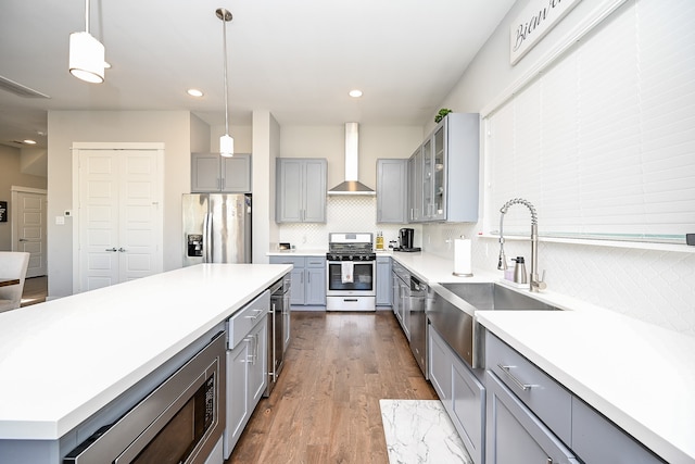 kitchen with pendant lighting, wall chimney range hood, appliances with stainless steel finishes, tasteful backsplash, and dark hardwood / wood-style flooring