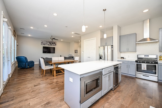 kitchen featuring dark hardwood / wood-style flooring, stainless steel appliances, ceiling fan, wall chimney range hood, and decorative light fixtures