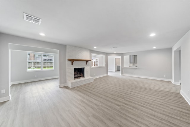 unfurnished living room featuring light wood-type flooring and a brick fireplace