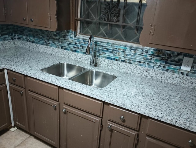 kitchen featuring light stone countertops, light tile patterned floors, tasteful backsplash, and sink