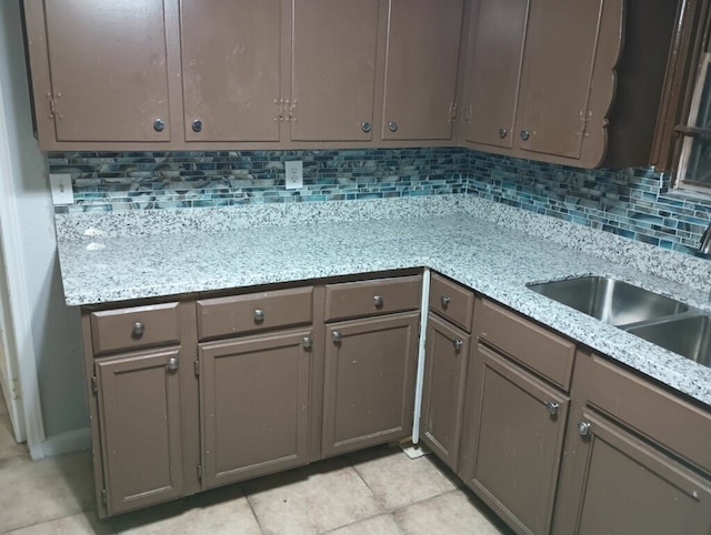 kitchen with decorative backsplash, light tile patterned floors, light stone countertops, and sink