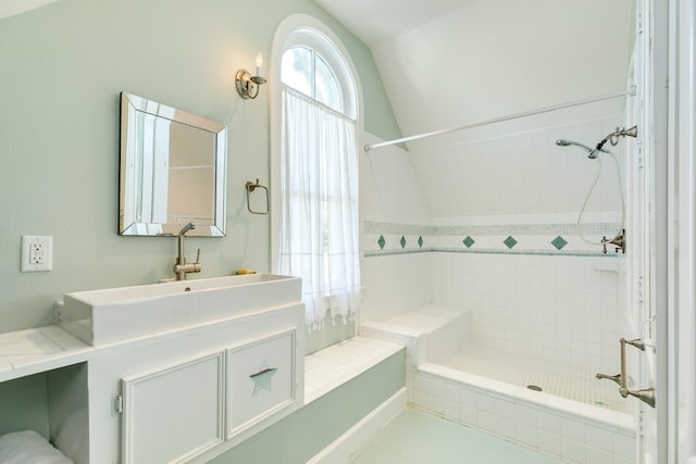 bathroom with tiled shower, vanity, and lofted ceiling