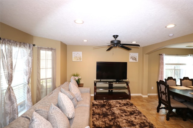 living room with light tile patterned floors, a textured ceiling, ceiling fan, and a healthy amount of sunlight