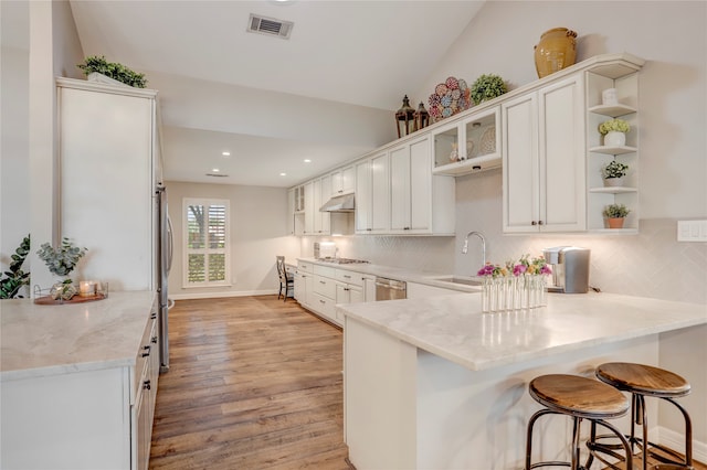 kitchen with kitchen peninsula, vaulted ceiling, sink, light hardwood / wood-style flooring, and white cabinetry