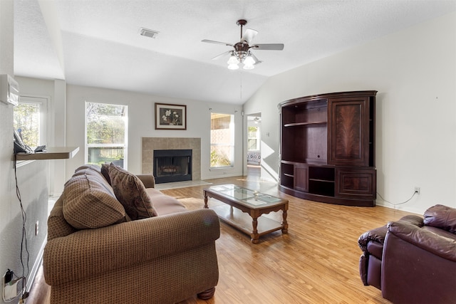 living room featuring a tile fireplace, vaulted ceiling, ceiling fan, a textured ceiling, and light hardwood / wood-style floors