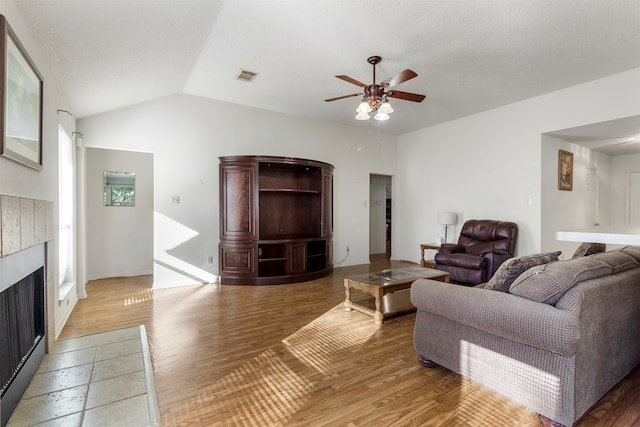 living room featuring hardwood / wood-style floors, ceiling fan, lofted ceiling, and a tile fireplace