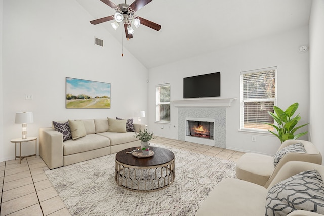 living room featuring high vaulted ceiling, ceiling fan, light tile patterned floors, and a tile fireplace