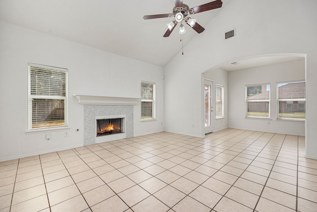 unfurnished living room with light tile patterned floors, high vaulted ceiling, a wealth of natural light, and a tiled fireplace