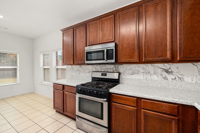 kitchen with decorative backsplash, light tile patterned floors, light stone countertops, and appliances with stainless steel finishes