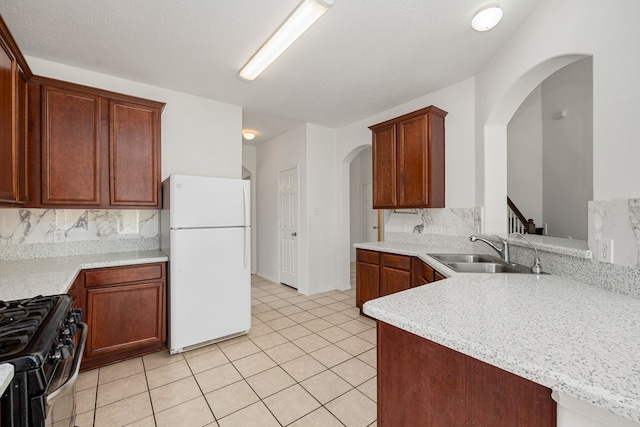 kitchen featuring gas stove, sink, white refrigerator, backsplash, and light tile patterned flooring