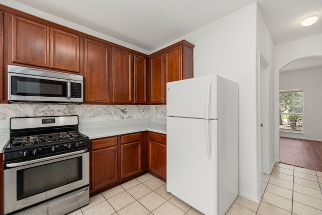 kitchen featuring tasteful backsplash, light tile patterned floors, stainless steel appliances, and a textured ceiling