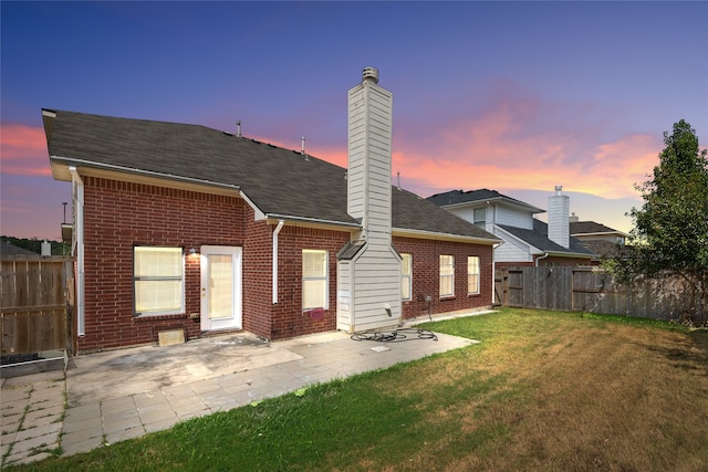 back house at dusk featuring a lawn and a patio area