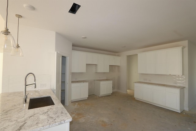 kitchen with a sink, stone countertops, white cabinetry, unfinished concrete floors, and hanging light fixtures