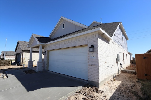 view of property exterior featuring an attached garage, brick siding, driveway, and a shingled roof