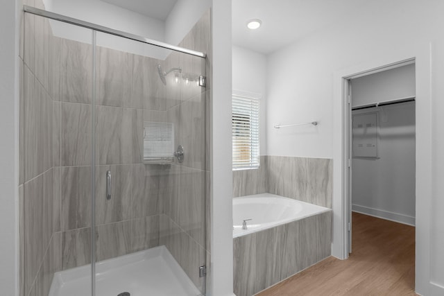 full bathroom featuring a spacious closet, a shower stall, wood finished floors, and a garden tub
