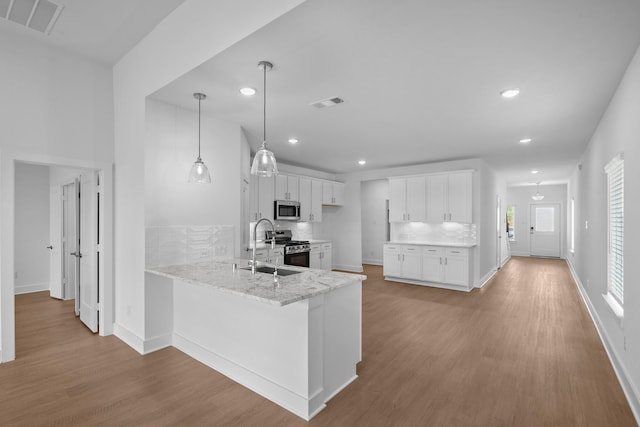 kitchen with white cabinets, stainless steel appliances, light wood-style flooring, and a peninsula