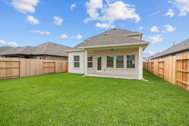 back of property featuring roof with shingles, a lawn, a patio area, brick siding, and a fenced backyard