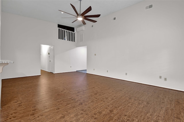 unfurnished living room with dark hardwood / wood-style flooring, a towering ceiling, a wall unit AC, and ceiling fan