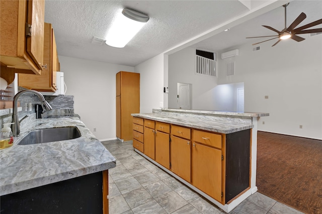 kitchen with ceiling fan, sink, kitchen peninsula, light hardwood / wood-style floors, and a textured ceiling