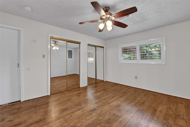 unfurnished bedroom with hardwood / wood-style floors, ceiling fan, a textured ceiling, and two closets