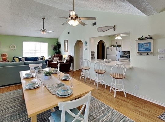 dining space with a textured ceiling, light hardwood / wood-style flooring, and vaulted ceiling