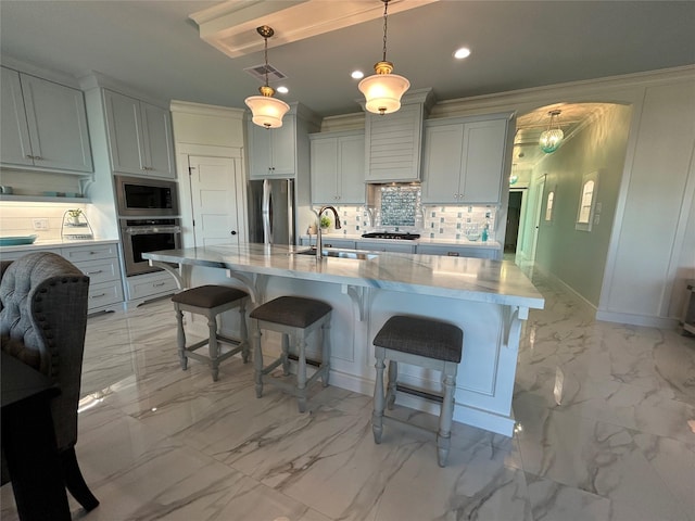 kitchen featuring sink, hanging light fixtures, an island with sink, appliances with stainless steel finishes, and tasteful backsplash