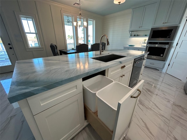 kitchen with stainless steel oven, a kitchen island with sink, white cabinets, sink, and light stone counters