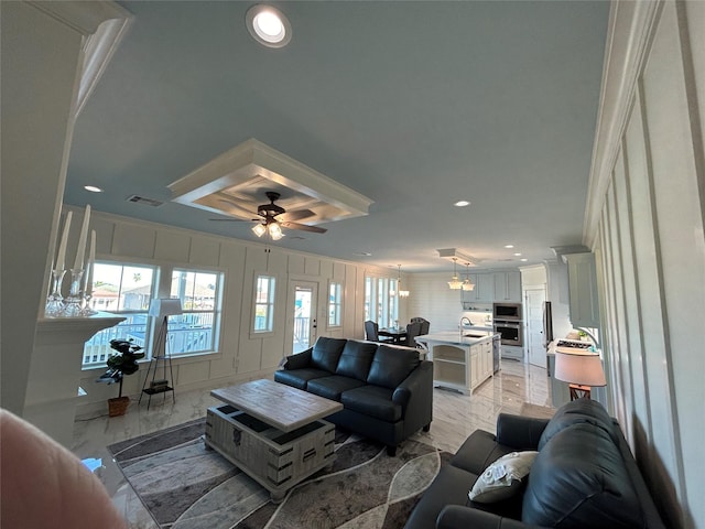 living room with ceiling fan, ornamental molding, and sink