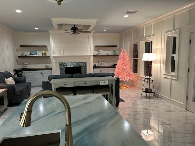 living room featuring a stone fireplace, ceiling fan, and crown molding