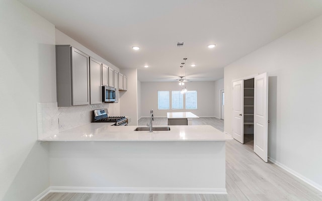 kitchen featuring gray cabinetry, sink, kitchen peninsula, appliances with stainless steel finishes, and light wood-type flooring