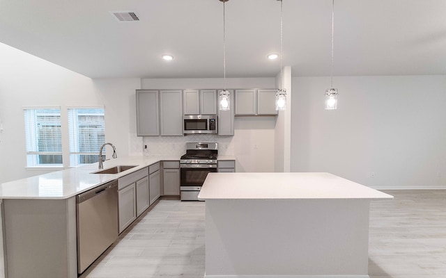 kitchen with pendant lighting, sink, appliances with stainless steel finishes, light hardwood / wood-style floors, and kitchen peninsula