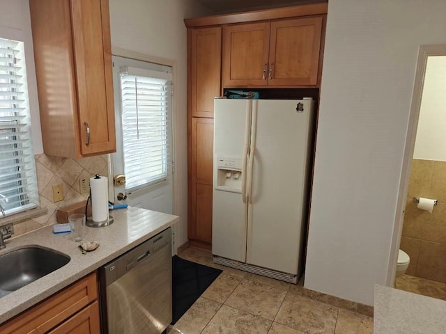 kitchen with tasteful backsplash, light stone counters, sink, white refrigerator with ice dispenser, and dishwasher